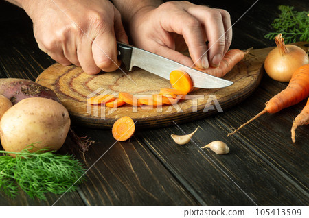 Slicing carrot by the hands of a chef on a cutting board to prepare delicious borscht for lunch at home. 105413509