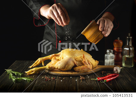 The chef preparing raw rooster in the kitchen. The cook adds salt to the cock before roasting. Preparing to cook Southern fried chicken The chef preparing raw rooster in the kitchen. The cook adds salt to the cock before roasting. Preparing to cook Southern fried chicken 105413531