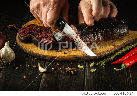 A knife in the cook's hand for cutting blood sausage for a very tasty dinner. Cooking a national dish with spices at home A knife in the cook's hand for cutting blood sausage for a very tasty dinner. Cooking a national dish with spices at home 105413554