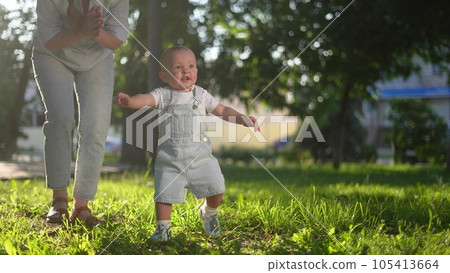 baby first steps in the park. happy family in the park on vacation. mother teaches baby son to take the first steps on the green grass in the summer in the park. happy family kid concept dream 105413664