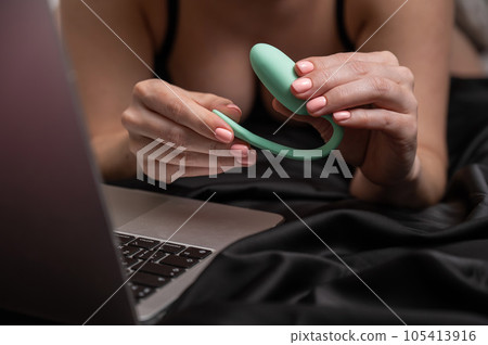 A woman lies on the bed and synchronizes the kegel machine with a laptop. A woman lies on the bed and synchronizes the kegel machine with a laptop. 105413916