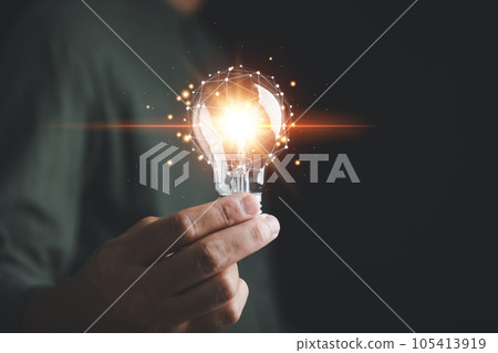 A man holds a bright light bulb, symbolizing creative new ideas, innovation, and inspiration. The concept of solution-oriented thinking and innovative technology is showcased in this creative moment. 105413919