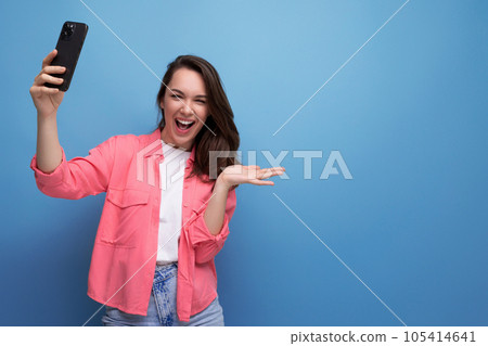 stylish brunette woman in a trendy shirt takes a selfie using a phone on a studio background stylish brunette woman in a trendy shirt takes a selfie using a phone on a studio background 105414641