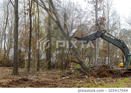 Worker is utilizing excavator to clear forest area for house foundation. Worker is utilizing excavator to clear forest area for house foundation. 105417044