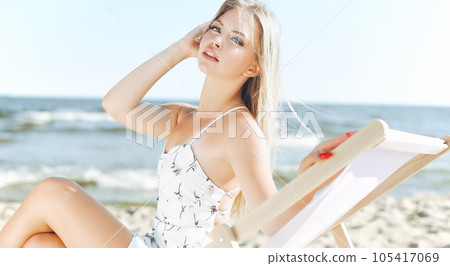 Happy blonde woman relaxing on a wooden deck chair at the ocean beach 105417069
