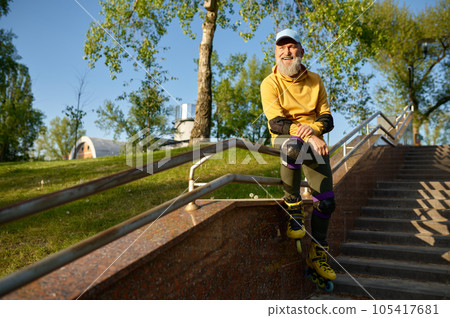 Senior man wearing roller skates rest sitting on stair railing Senior man wearing roller skates rest sitting on stair railing 105417681