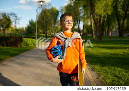 Portrait of little boy carrying helmet and skateboard over street background 105417689