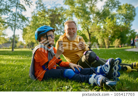 Happy grandpa and grandchild eating ice-cream after roller skating 105417703