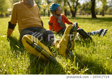 Happy man and boy rollerskaters rest on grass filed in park 105417724