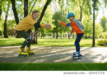 Grandfather teaching grandson riding roller skates in city park Grandfather teaching grandson riding roller skates in city park 105417729