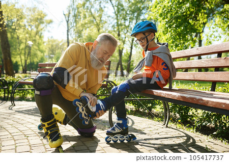 Father helping son to put on roller skates in urban park 105417737