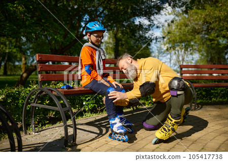 Grandfather helping grandson to put on roller skates in urban park 105417738