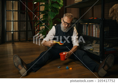 Funny senior businessman playing toys while sitting on floor 105417752