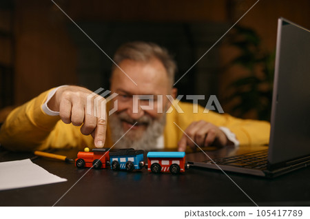 Selective focus portrait with senior man playing with toy train at workplace Selective focus portrait with senior man playing with toy train at workplace 105417789