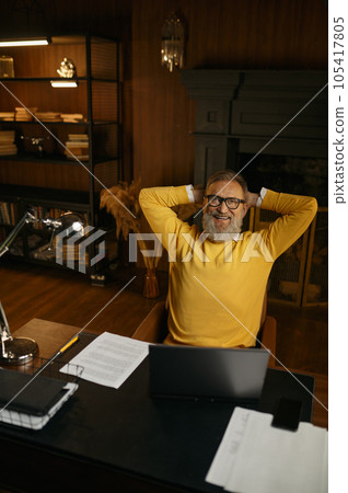 Excited mature man feeling satisfaction sitting at table in home office 105417805