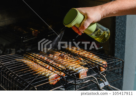 Male hand watered with olive oil, spices fish, baked on a grill. Male hand watered with olive oil, spices fish, baked on a grill. 105417911