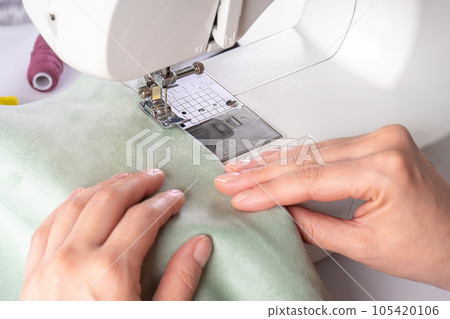 Female hands stitching green fabric on modern sewing machine at workplace in atelier Female hands stitching green fabric on modern sewing machine at workplace in atelier 105420106