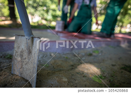 In the foreground, a shovel stuck in the ground and construction workers in the background. 105420868