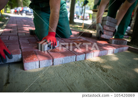 A skilled construction worker lays red paving stones on a sidewalk. 105420869