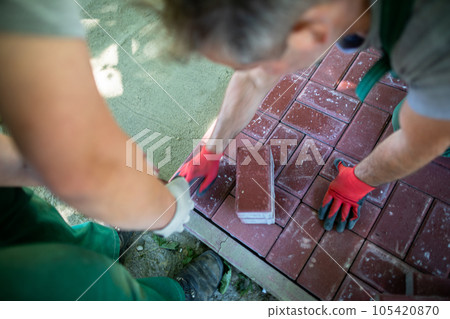 One worker brings in the paving stones and the other lays them evenly and accurately. 105420870