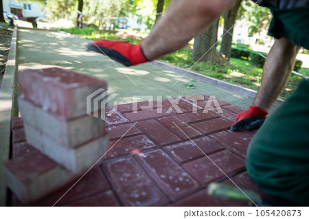 A construction worker kneels to lay paving stones on a sunny day. A construction worker kneels to lay paving stones on a sunny day. 105420873