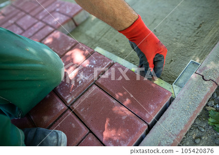 During the laying of paving blocks, the worker checks with a protractor, the correctness of the workmanship. 105420876