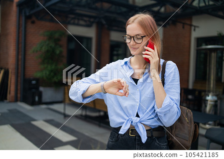 Angry irritated young business woman holding mobile phone and looks at his watch at the blurry business center building Angry irritated young business woman holding mobile phone and looks at his watch at the blurry business center building 105421185
