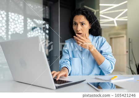 Upset businesswoman at workplace received bad news, online notification message. Hispanic woman working inside the office with a laptop. Upset businesswoman at workplace received bad news, online notification message. Hispanic woman working inside the office with a laptop. 105421246
