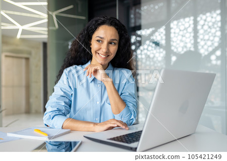 Young beautiful thinking woman smiling and looking out the window, businesswoman smiling at workplace satisfied with achievement results, Latin American woman using laptop at work. 105421249