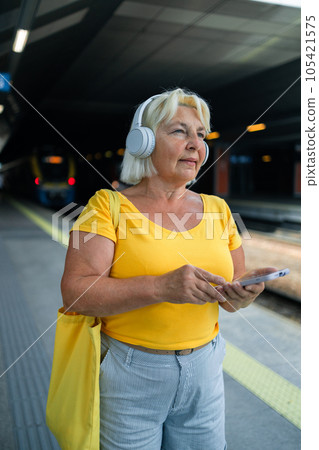Happy 50s senior woman waiting for the train on station platform and using smartphone. 105421575