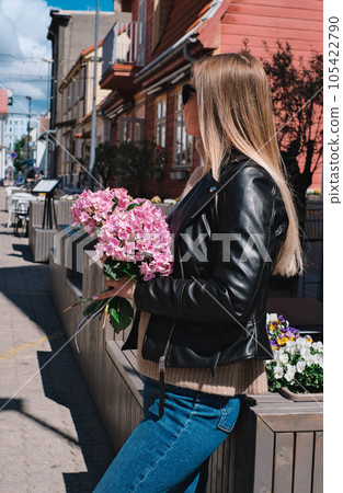 Beautiful caucasian girl with blond hair in a gray coat and blue jeans with a bouquet of pink hydrangeas Beautiful caucasian girl with blond hair in a gray coat and blue jeans with a bouquet of pink hydrangeas 105422790