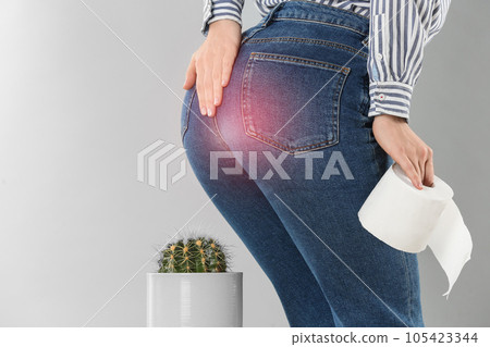 Woman with toilet paper sitting down on cactus against light grey background, closeup. Hemorrhoid concept Woman with toilet paper sitting down on cactus against light grey background, closeup. Hemorrhoid concept 105423344