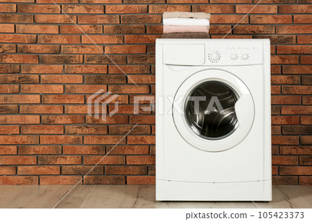 Modern washing machine with stack of towels near brick wall, space for text. Laundry day 105423373