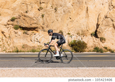 Side view of a professional cyclist in black sportswear riding bike at mountain 105423406