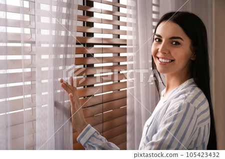 Woman near window with beautiful curtains at home 105423432