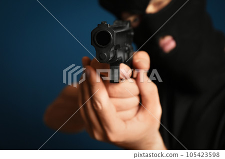 Man in mask holding gun against dark blue background, focus on hands 105423598
