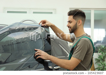 Worker tinting car window with foil in workshop 105423607