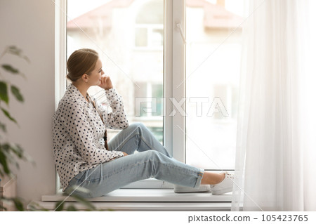 Beautiful young woman looking out of window at home Beautiful young woman looking out of window at home 105423765
