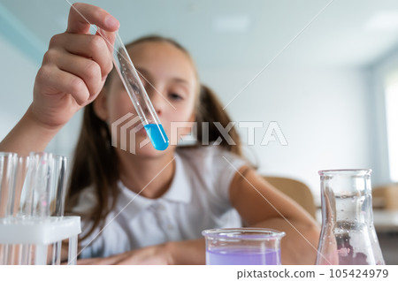 A schoolgirl conducts experiments in a chemistry lesson. Girl pouring colored liquids from a beaker. A schoolgirl conducts experiments in a chemistry lesson. Girl pouring colored liquids from a beaker. 105424979