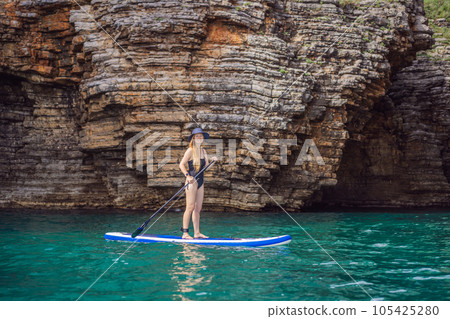 Young women Having Fun Stand Up Paddling in blue water seaamong the rocks in Montenegro. SUP Young women Having Fun Stand Up Paddling in blue water seaamong the rocks in Montenegro. SUP 105425280