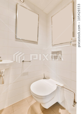 a white toilet in a bathroom with two mirrors on the wall above it and a sink next to the toilet 105426553
