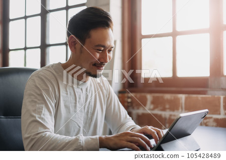 Happy man doing work online from his tablet in his own office. 105428489