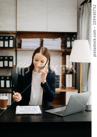 Confident business expert attractive smiling young woman typing laptop ang holding digital tablet on desk in office.. 105430752