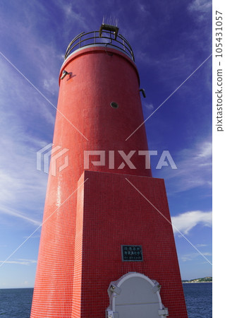 A red lighthouse standing on a breakwater with a blue sky background A red lighthouse standing on a breakwater with a blue sky background 105431057