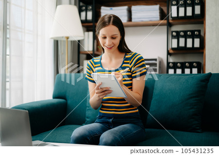 Confident Caucasian woman with a smile standing holding notepad and tablet in living room on the sofa at office 105431235