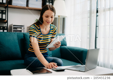 Confident Caucasian woman with a smile standing holding notepad and tablet in living room on the sofa at office 105431236