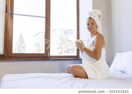 Woman in bath towel and towel on hair holding a cup and smiling 105431681