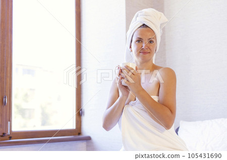 Woman in bath towel and towel on hair holding a cup and smiling 105431690