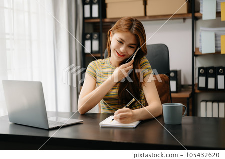 Business asian woman Talking on the phone and using a laptop with a smile while sitting at home office. 105432620
