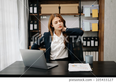 Overworked young Asian businesswoman office worker suffering from neck pain after had a long day at her office table. office syndrome concept 105433127